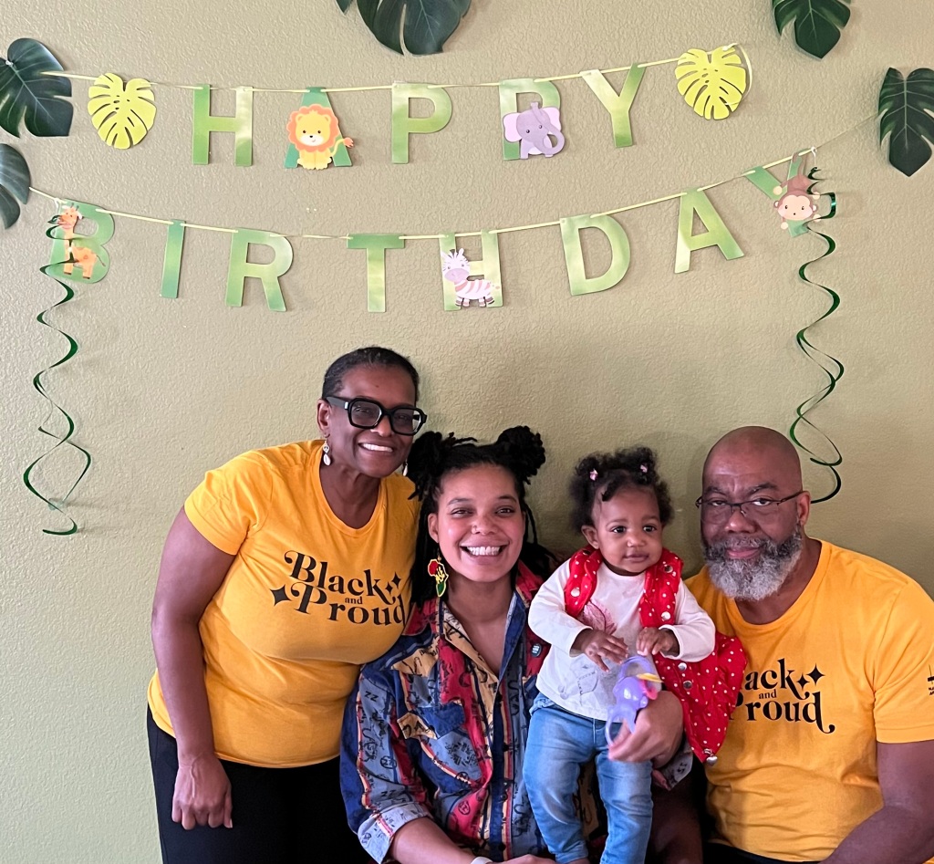 Photo of Tonya Cross visionary of Accented Glory with her husband, daughter, and granddaughter at her granddaughter's first birthday party.